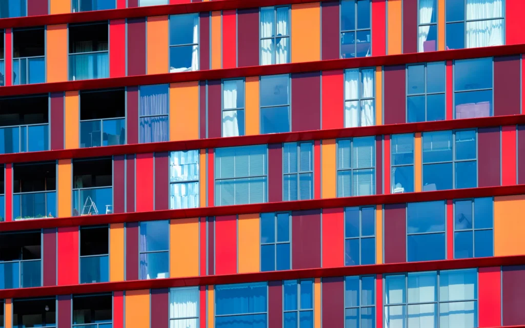 Façade d’immeuble moderne aux panneaux rouges, orange et bleus, avec de nombreuses fenêtres
