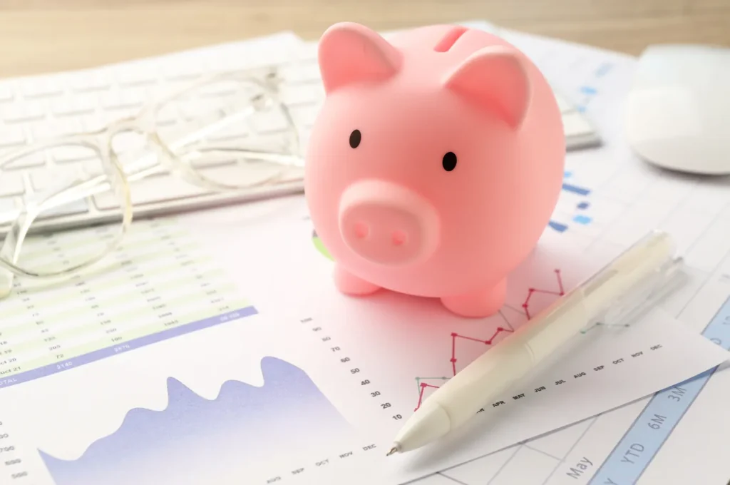 Tirelire rose posée sur des graphiques financiers imprimés, avec un stylo et des lunettes