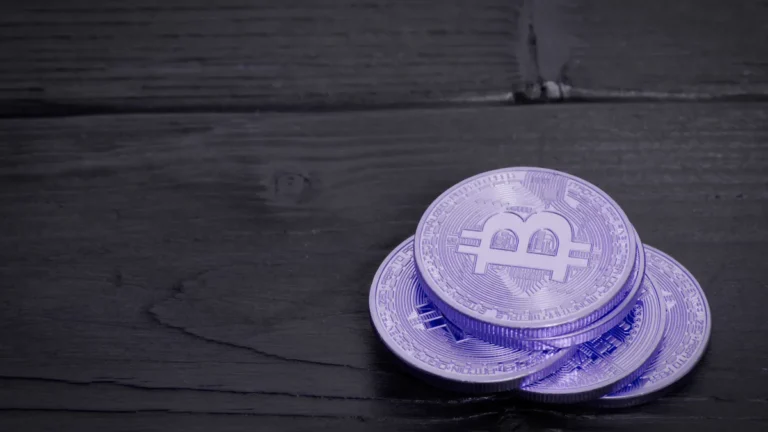 Trois pièces de bitcoin violettes posées sur un bois sombre