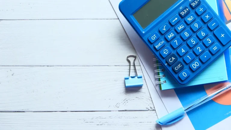Calculatrice bleue, carnet, trombone et stylo sur une table en bois blanc