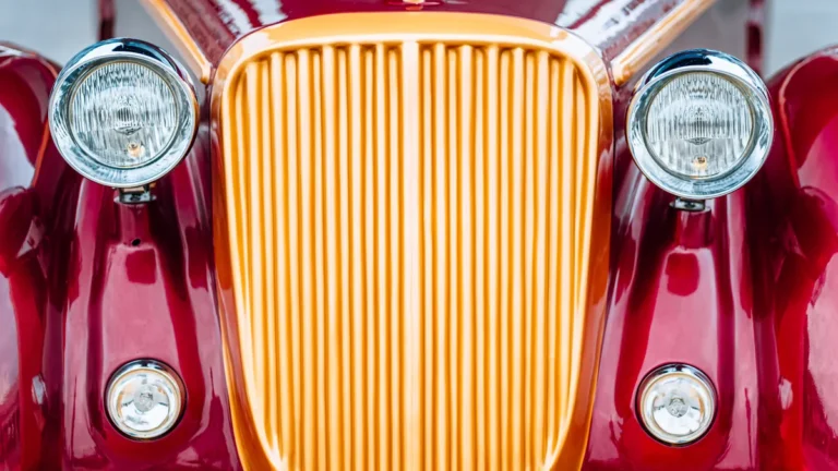 Calandre dorée et phares chromés d’une voiture ancienne rouge